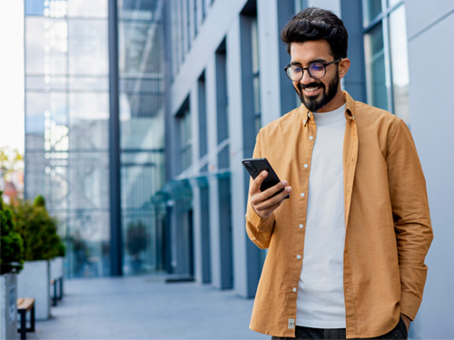 homem jovem em pé na rua mexendo no celular e sorrindo