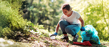 Pessoa recolhendo lixo ao ar livre com luvas e um saco grande de reciclagem.