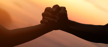 Duas mãos entrelaçadas diante de um pôr do sol.