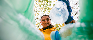 Pessoa vista de baixo descartando garrafas plásticas em um recipiente.