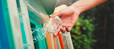 Mão descartando uma garrafa plástica transparente em um coletor colorido de reciclagem.