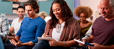 Grupo de pessoas sentadas em uma sala participando de uma atividade com cadernos e tablets.