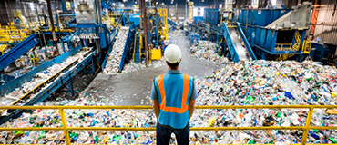 Trabalhador observando grande área de triagem repleta de resíduos em instalação industrial.