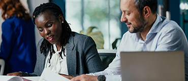 Duas pessoas em um ambiente de escritório analisando documentos juntas.
