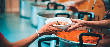 Mão entregando um prato de comida em uma ação de distribuição de refeições.